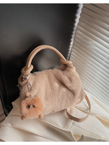 Detail einer beigen Plüschhandtasche mit Ledergriff und süßem Pelz-Anhänger