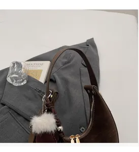 Dettaglio borsa hobo marrone scuro con cerniera e ciondolo a pompon di pelliccia bianca