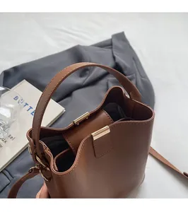 Detail of a brown leather bucket bag with gold hardware on a grey blazer backdrop