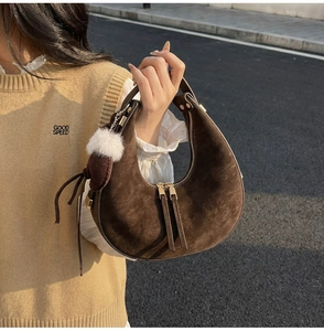 Dettaglio di una borsa a mezzaluna in camoscio marrone con ciondolo a pompon bianco