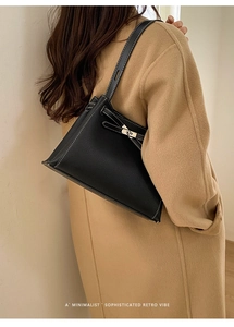Détail du sac trapèze en cuir noir avec coutures blanches contrastées et fermoir argenté