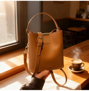 Detail of a brown leather bucket bag with top handle and gold hardware in a cafe setting