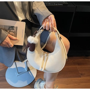 Dettaglio della borsa a mezzaluna bianco sporco con doppia zip e ciondolo in peluche