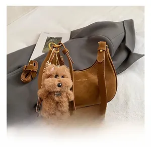 Dettaglio borsa hobo in pelle scamosciata marrone con logo dorato e ciondolo a cane di peluche