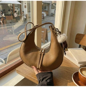Dettaglio di una borsa hobo marrone con doppia cerniera e ciondolo in peluche in un caffè