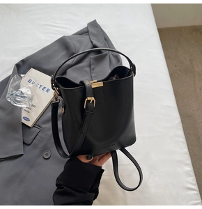 Detail of black matte bucket bag with gold hardware on a gray blazer setting