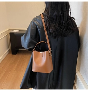 Detail of brown leather bucket bag with logo and thin shoulder strap over wood floor