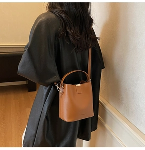Detailed view of brown leather bucket bag with brand logo and detachable shoulder strap