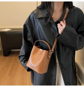 Brown leather bucket bag with adjustable strap styled on a black trench coat for work
