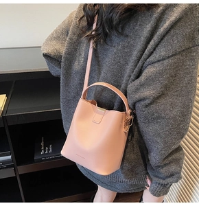 Detailed view of a pink matte leather bucket bag with top handle and adjustable strap on model
