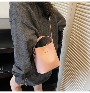 Detail of pink leather bucket bag with top handle and crossbody strap on casual model