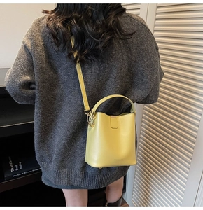 Detail of yellow leather bucket bag featuring adjustable strap and metallic hardware