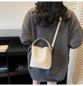 Detail of cream leather bucket bag with top handle and adjustable shoulder strap worn by model