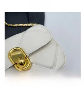 Detail shot of a white quilted crossbody bag with a golden oval metal twist lock