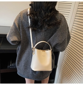 Rear view of a white leather bucket bag with top handle and adjustable strap on model