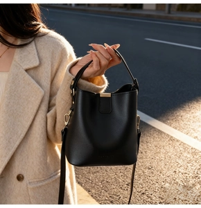 Close-up of black bucket bag with golden hardware on a model in a beige wool coat
