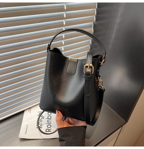 Detail of black leather bucket bag with wide handle, gold hardware and long strap