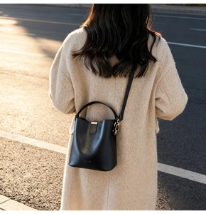 Detail of minimalist black bucket bag styled with a wool coat in warm sunset street light