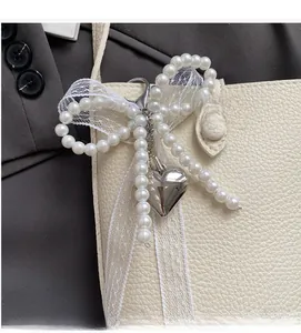 Elegant pearl bow charm with metal heart and lace ribbon on a stylish bucket bag