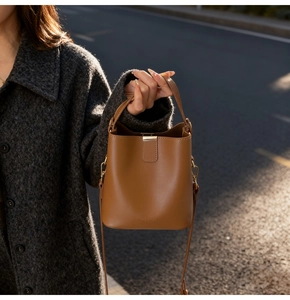 Detail of a brown leather bucket bag with gold clasp and brand logo in soft natural sunlight