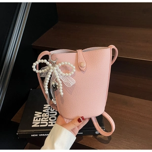 Detail of pink faux leather bucket bag with pearl bow and lace charm on wooden stairs