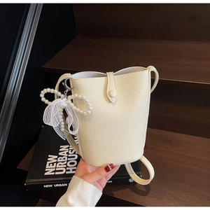 Detail of cream bucket bag with litchi texture, pearl bow charm, and lace ribbon