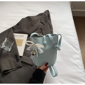 Detail of light blue bucket bag with pebble leather, pearl bow, and heart charm