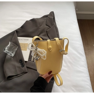 Detail of yellow bucket bag with lychee texture featuring pearl bow and silver heart charm