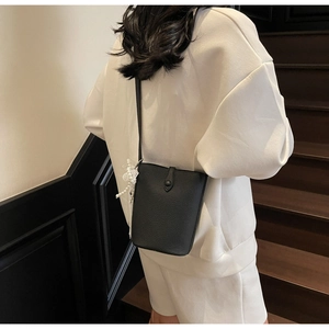 Detail of black lychee grain bucket bag with pearl bow charm worn on the shoulder