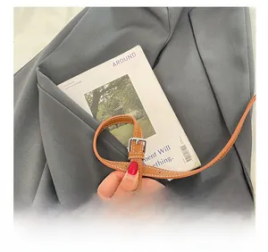 Détail d'une bandoulière réglable en cuir marron avec boucle en métal argenté et surpiqûres
