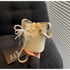 Detail of cream bucket bag with lychee texture, pearl bow charm, and lace trim detail