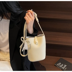 Chic off-white bucket bag with pearl bow charm held by model on dark background