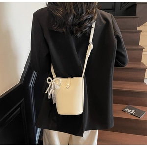 Chic cream bucket bag with pearl bow charm worn over the shoulder on a model