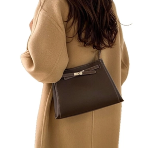 Sac à bandoulière en cuir marron foncé avec boucle et design trapèze sur manteau camel