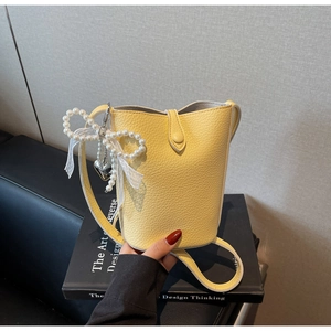 Detail of yellow bucket bag with lychee texture and pearl bow charm accessory