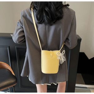Close-up of yellow bucket bag with pearl lace bow charm worn by a model in a grey coat