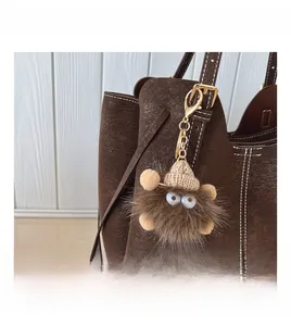 Dettaglio del ciondolo mostro di peluche marrone con cappello di maglia su borsa di pelle