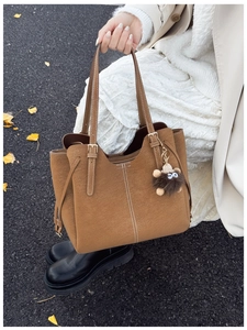 Dettaglio borsa tote in pelle scamosciata marrone con cuciture bianche e ciondolo peluche