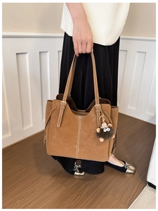 Dettaglio borsa tote in pelle marrone con cuciture bianche e ciondolo di peluche