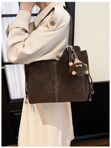 Dettaglio della borsa tote in pelle scamosciata marrone con cuciture a contrasto e charm