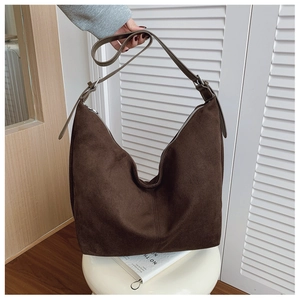 Detail of dark brown suede hobo bag with adjustable strap on a white stool