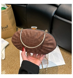 Détail de la pochette ovale marron avec poignée dorée et fermoir bijou sur fond mode