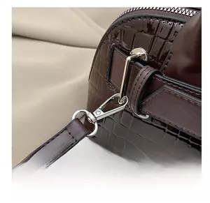 Close-up of silver metal hooks and glossy crocodile pattern leather on a crossbody bag