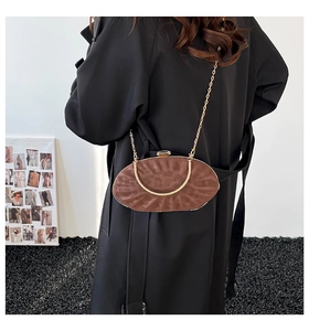 Pochette ovale marron avec bandoulière chaîne portée par un mannequin sur fond sobre