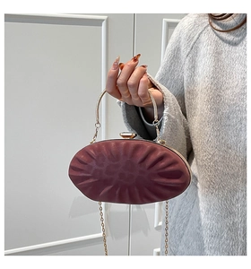 Détail d'une pochette ovale bordeaux avec texture plissée, poignée dorée et chaîne en métal