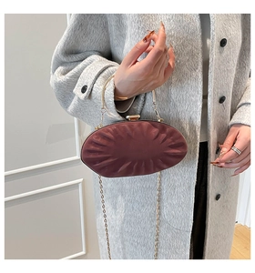 Détail d'une pochette ovale bordeaux avec texture plissée et poignée ronde dorée