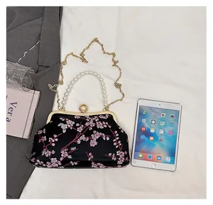 Detailed size comparison of embroidered satin bag with pearl handle and iPad mini