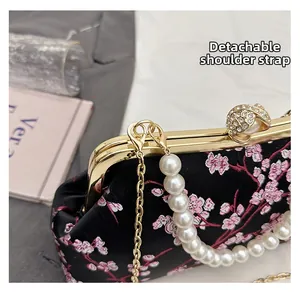 Detail of black satin crossbody bag featuring pink cherry blossom embroidery and pearl strap