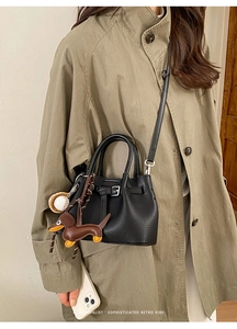 Detail der schwarzen Leder-Tasche mit Gürtelschnalle und Hund-Anhänger am Model gezeigt