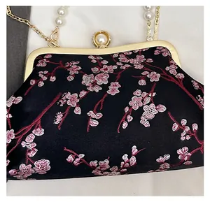 Close-up of pink cherry blossom embroidery on black satin with pearl clasp detail
